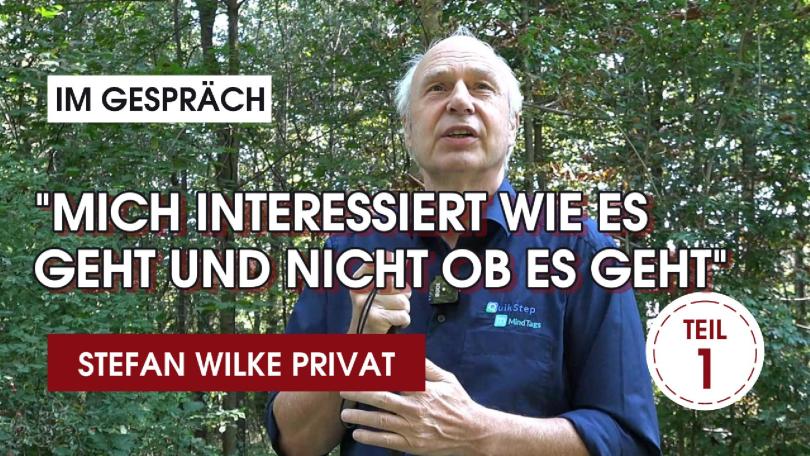 Auf dem Bild ist ein Mann, mit weißen Haaren, draußen umgeben von Bäumen zu sehen. Er trägt ein dunkelblaues Hemd. Auf dem Bild steht in großen weißen Buchstaben :"MICH INTERESSIERT WIE ES GEHT UND NICHT OB ES GEHT". Darüber steht in einem kleinen weißen Kasten "IM GESPRÄCH". Ganz unten im Bild ist ein roter Kasten mit weißem Text: "STEFAN WILKE PRIVAT" zu sehen. Unten rechts im Bild ist ein weißer Kreis mit rotem Rand, in dem TEIL 1 steht.